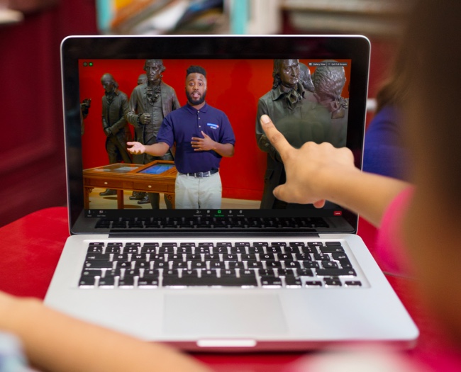 Student touching a laptop computer displaying an online class